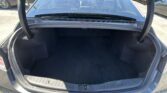 Open trunk of a dark sedan showing a spacious empty cargo area with folded rear seats visible through the rear window and bright daylight outside.