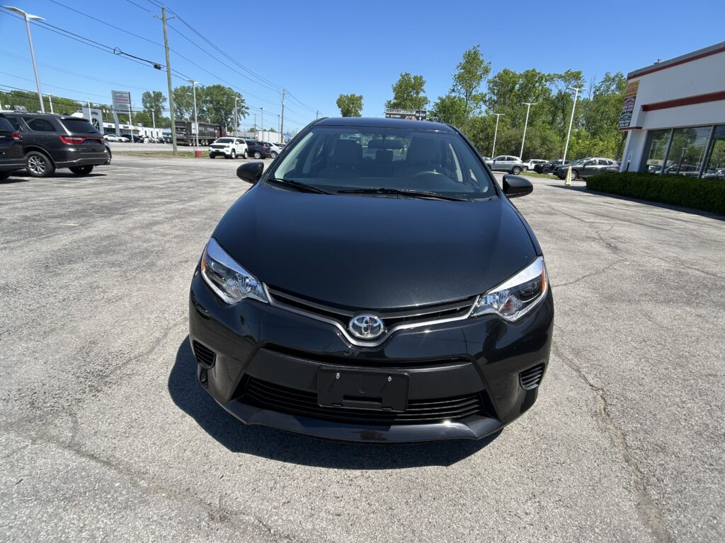 Front view of a black Toyota SUV parked in a parking lot with a dealership building on the right and other cars in the background under a clear blue sky.