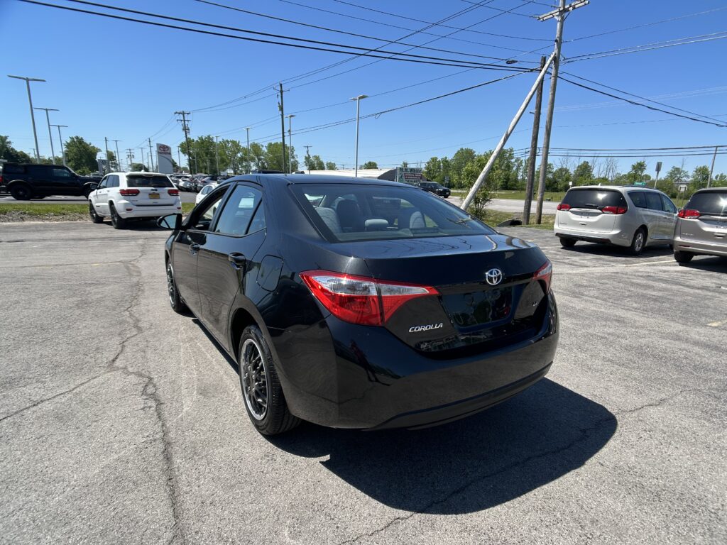 Rear three-quarter view of a black Toyota Corolla in a crowded parking lot with other vehicles and power lines overhead to the blue sky.