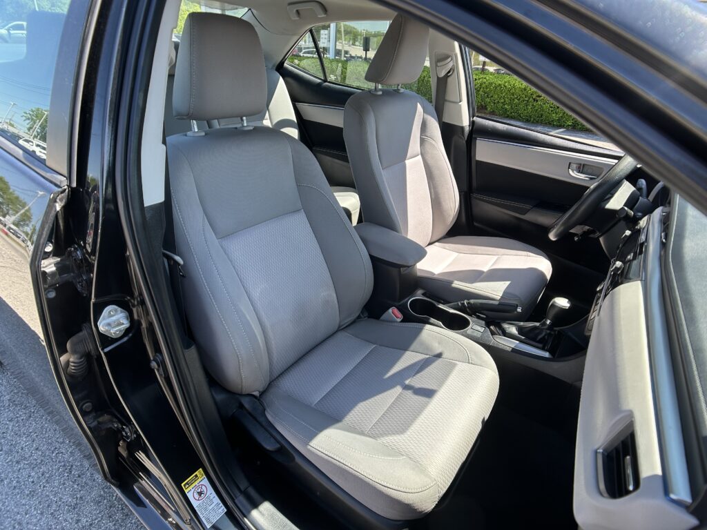 Front passenger and driver seats in a car, gray fabric upholstery, with the driver's door open showing the interior layout and center console.
