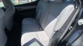 Rear seat interior of a gray fabric sedan with three seats and headrests, seen through an open door while parked outside.