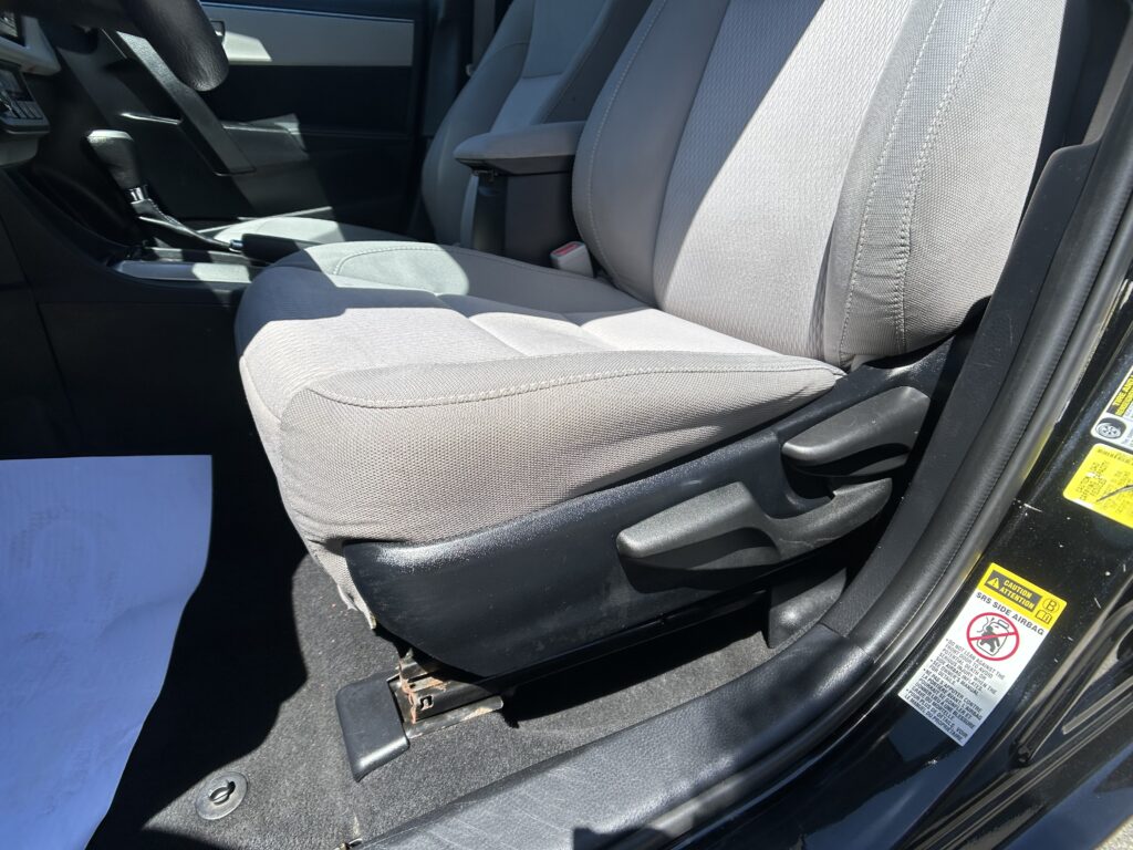 Interior of a car's front cabin showing gray cloth seats, center console with an armrest, and the gear shifter to the left of the passenger seat.