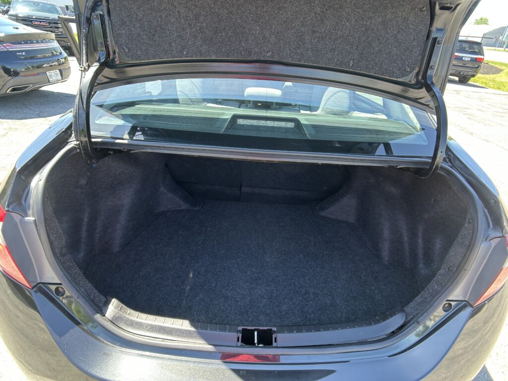 Open hatchback trunk of a dark sedan with empty carpeted cargo space and rear window visible