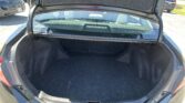 Open hatchback trunk of a dark sedan with empty carpeted cargo space and rear window visible