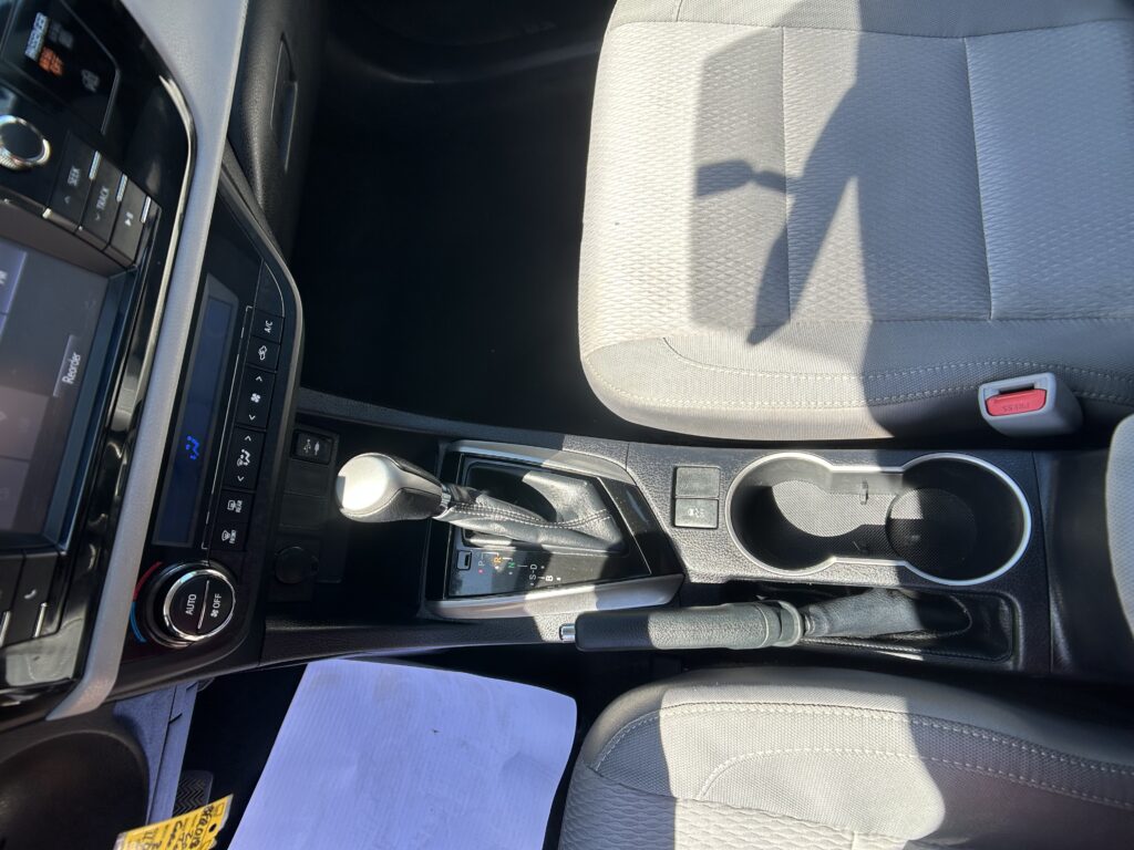 Interior of a car showing the center console with gear shifter, cup holders, and a gray passenger seat nearby.
