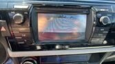 Rearview camera feed on the car's center screen showing blue parking guide lines for backing up, with dashboard controls around it.