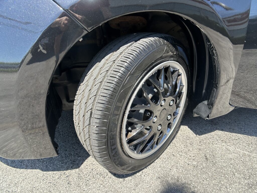 Close-up of a car's front wheel and tire in the wheel well, showing a black alloy rim and tread pattern on the tire.
