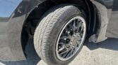 Close-up of a car's front wheel and tire in the wheel well, showing a black alloy rim and tread pattern on the tire.