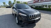 Front-left view of a black Jeep SUV parked in a lot in front of an auto dealership with bold red letters on the building saying E-Z LOAN AUTO SALES.