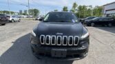 Front view of a black Jeep SUV parked in a dealership lot with other cars and a building in the background.