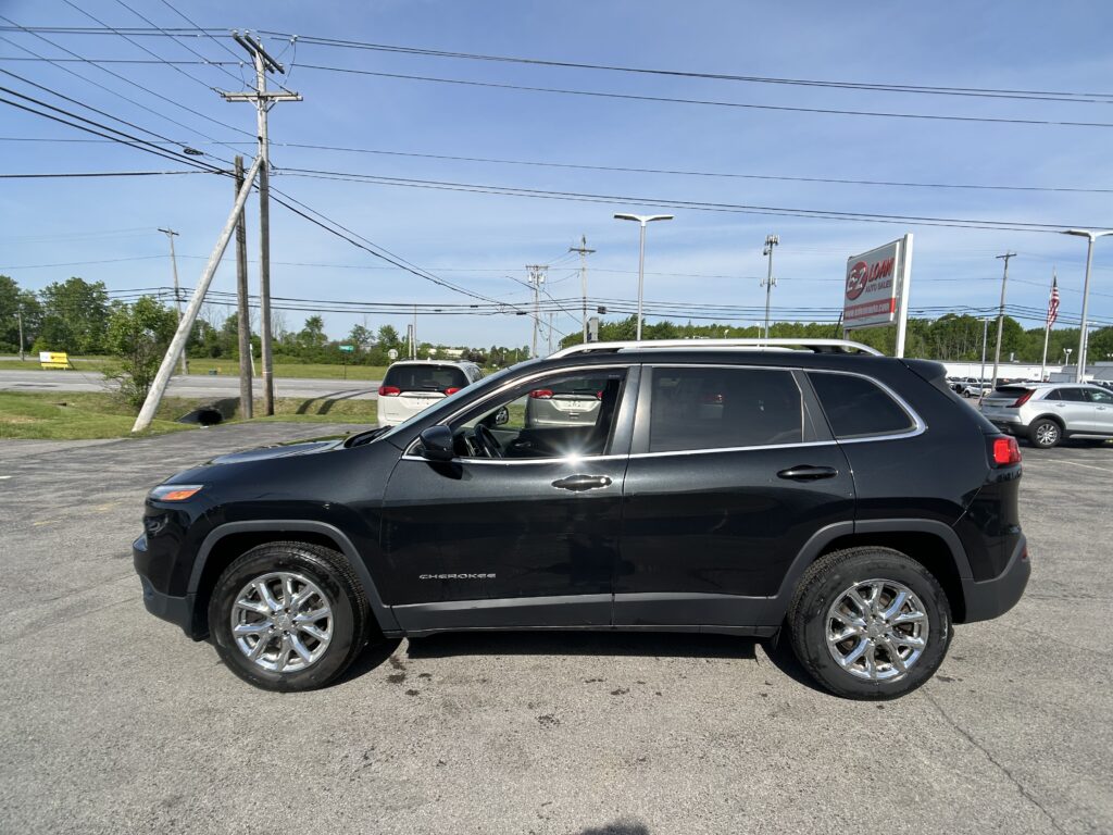 Black Jeep Cherokee parked in a dealership lot with power lines and poles in the background.