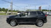 Black Jeep Cherokee parked in a dealership lot with power lines and poles in the background.