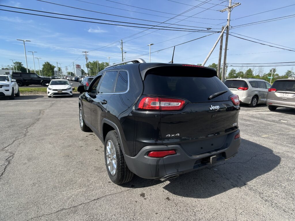 Rear view of a black Jeep SUV in a car dealership lot, with other vehicles and a Toyota sign in the background.