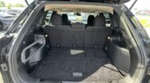 Cargo area of a black SUV with rear hatch open and third-row seats up, empty trunk ready for loading nearby parked cars.