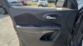 Open car door interior showing control panel and door handle; outside parking lot with multiple cars visible in background