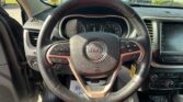 Inside view of a Jeep steering wheel and dashboard, with a sunny car lot visible through the windshield behind.