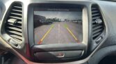 Car dashboard screen showing rearview camera with green, yellow, and red guiding lines in a parking lot scene.