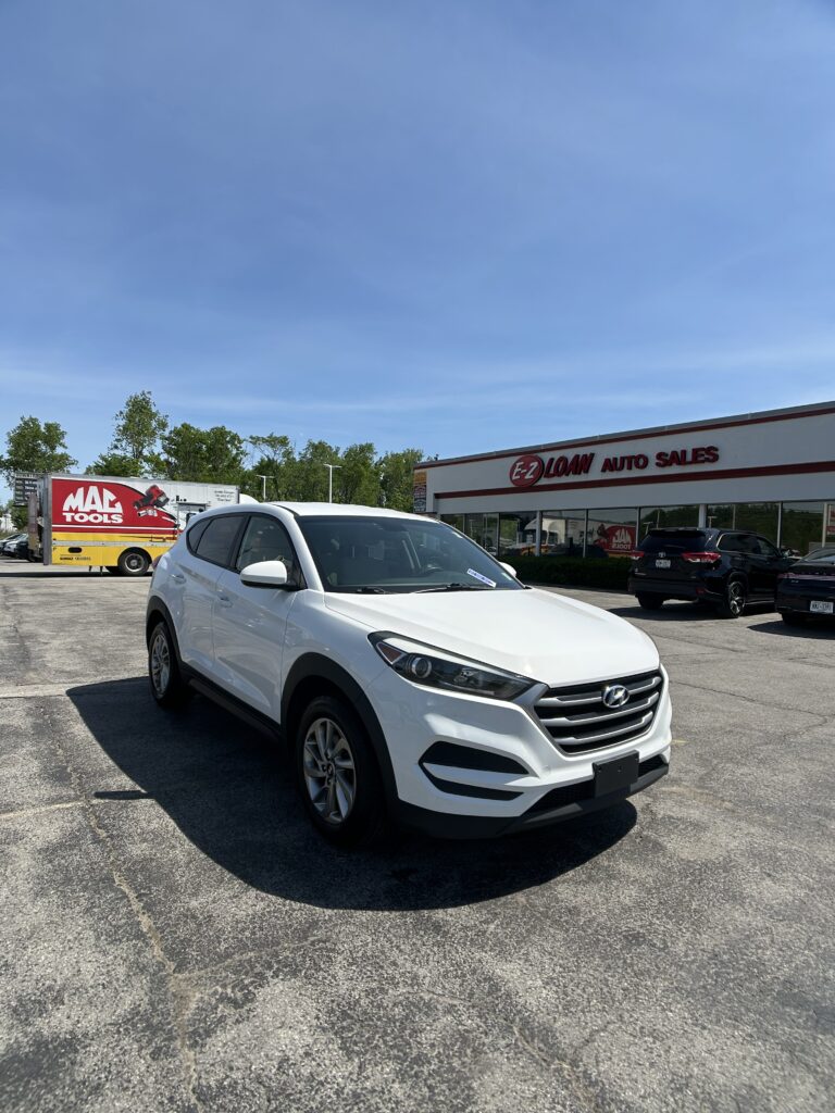 White Hyundai SUV parked in front of E-Z Loan Auto Sales on a sunny day in a dealership lot.