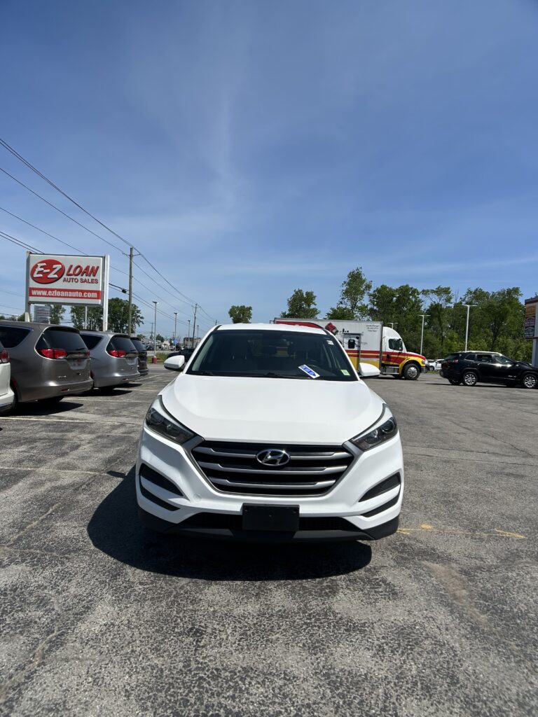 Front view of a white Hyundai SUV parked in a dealership lot, with an E-Z LOAN Auto Sales sign visible in the background on the left.