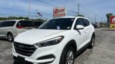 White Hyundai SUV in a car dealership lot with a red EZ LOAN Auto Sales sign in the background and an American flag nearby.
