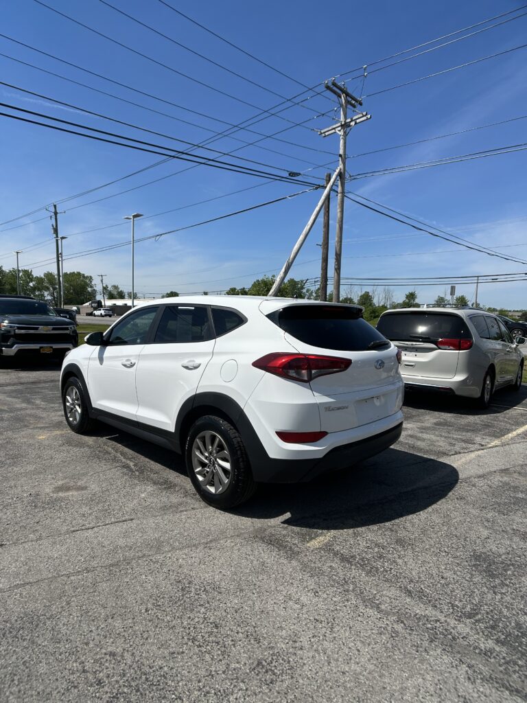 White Hyundai Tucson SUV parked in a lot with another car nearby under a blue sky and overhead power lines.