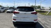 Rear view of a white Hyundai Tucson in a parking lot with other cars and a clear blue sky above, power lines overhead.