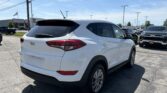 Rear three-quarter view of a white Hyundai SUV in a dealership parking lot on a sunny day, with power lines overhead and other vehicles in the background.
