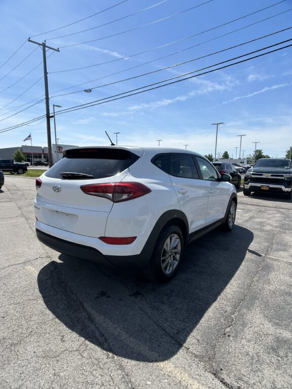 Rear three-quarter view of a white Hyundai SUV in a dealership parking lot on a sunny day, with power lines overhead and other vehicles in the background.