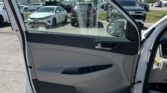 Open white car door showing the light-gray interior and view of a parking lot with parked cars outside