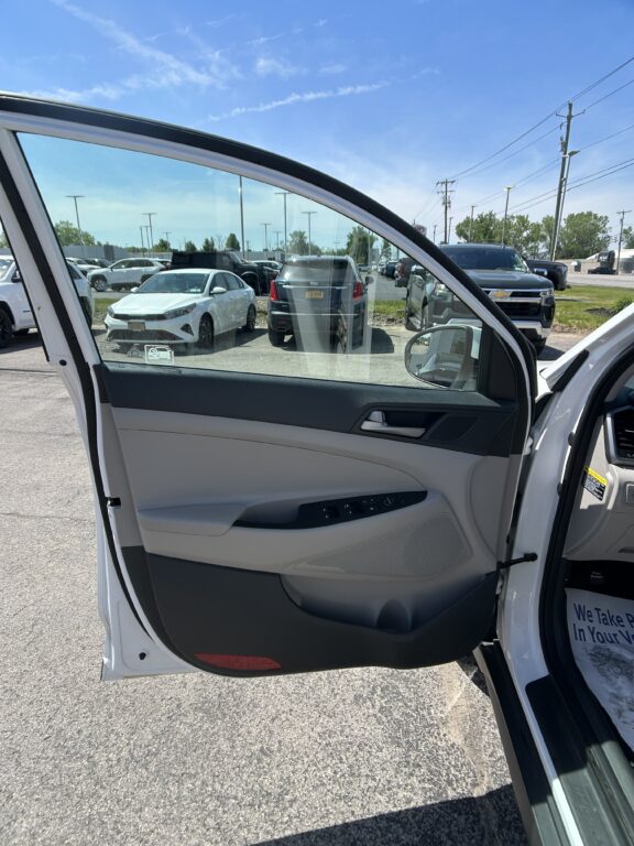 Open white car door showing the light-gray interior and view of a parking lot with parked cars outside