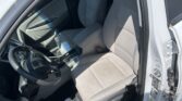 Interior of a white car with the driver’s door open, showing light gray front seats, steering wheel, and center console.