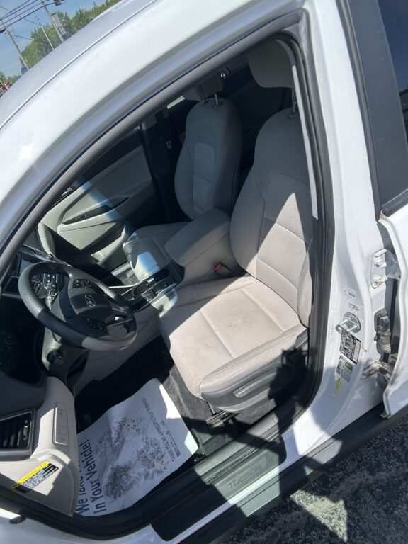 Interior of a white car with the driver’s door open, showing light gray front seats, steering wheel, and center console.