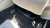 Inside a car's front footwell: beige seat fabric, dark floor mat, and the exposed seat rail near the lower edge of the seat.