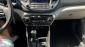 Driver's-eye view of a car cabin: center touchscreen showing 11:15 AM, gear shifter, and cupholders in the console.