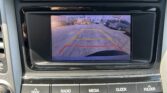 Car's infotainment screen showing the rearview camera view with yellow and red guiding lines in a parking lot
