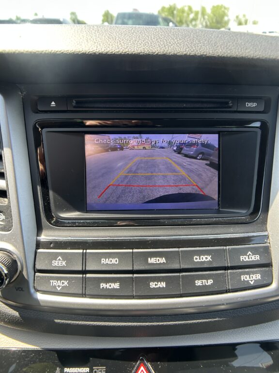 Car's infotainment screen showing the rearview camera view with yellow and red guiding lines in a parking lot