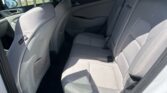 Back row of a gray SUV with fabric seats, headrests, and visible seat belts, viewed from open rear door.