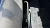 Car interior: gray upholstered seat with a metal handbrake lever between the seats and a dark floor mat.