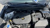 Open car hood revealing engine bay with battery, coolant tank, and hoses Visible on left is the coolant reservoir and various hoses.