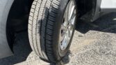 Front-right tire and wheel of a white vehicle in the wheel well, parked on asphalt.