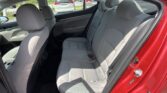 Interior of a red sedan showing gray rear bench seats with headrests and seat belts, front seats visible, parked cars outside through the windows.
