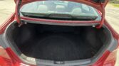 Open red sedan trunk showing a spacious black carpeted cargo area and rear seats visible through the rear window.