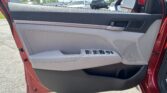 Interior of a car door showing the armrest, window controls, and speaker panel in gray and black, with a red door frame outside.