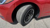 Close-up of a red car showing the front fender, headlight area, and a black alloy wheel with tire.