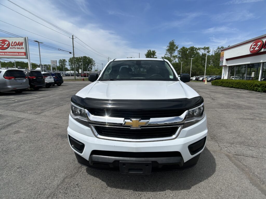 Front view of a white Chevrolet pickup parked in a car dealership lot, with the EZ Auto Sales building in the background and other vehicles nearby.