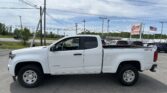White Chevrolet Colorado pickup in a parking lot, with power lines overhead and an E-Loan Auto Sales sign in the background and an American flag nearby.