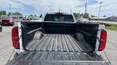 Open pickup truck bed seen from the back, with a textured bed liner and surrounding parking lot and other vehicles under a blue sky.