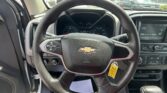 Driver’s view of a Chevrolet steering wheel, instrument cluster, and in-dash display; a parking lot is visible through the windshield.