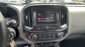 View of a car's center console and dashboard from the driver's seat: touchscreen radio displaying AM stations and climate controls below, with the steering wheel to the left and keys in the ignition.