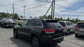 Black Jeep Grand Cherokee in a parking lot with other cars and tall utility poles overhead against a blue sky.